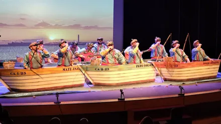 Imagen del escenario con unas barcas como de juguete y cantando las chirigotas.