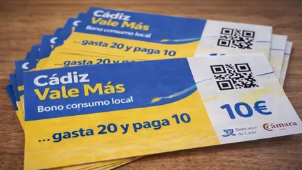 Sobre una mesa de madera un taco de bonos de "Cádiz Vale Más" en colores amarillo y azul.