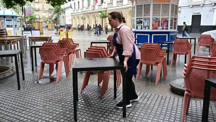 Una trabajadora de hostelería mueve y organiza mesas y sillas en la terraza de un bar situada en la plaza de San Juan de Dios, en el centro de Cádiz. La escena refleja una terraza parcialmente vacía y un momento de menor actividad tras las fiestas navideñas.