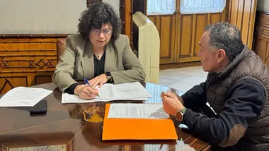 Carmen Álvarez en una mesa de madera firmando unos documentos.