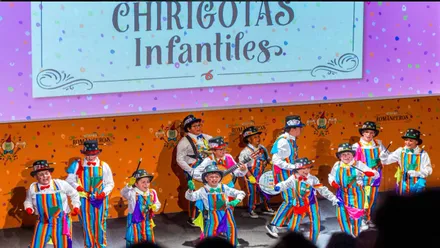 Niños en el escenario participando en el Carnaval Infantil, visten trajes de rayas de muchos y vistosos colores.