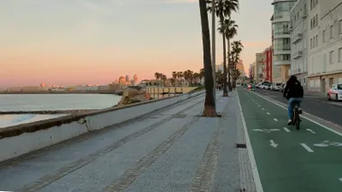 Una mujer circula en su bici por el Carril bici del Paseo MArítimo de Cádiz bajo un cielo despejado