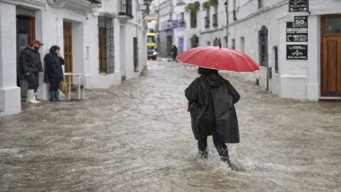 Inundaciones, una mujer con paraguas rojo y chubasquero cruza la calle en Grazalema.