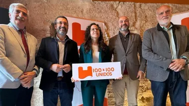 Laura Román sosteniendo un cartel blanco con letras naranjas que pone "100x100 Unidos".