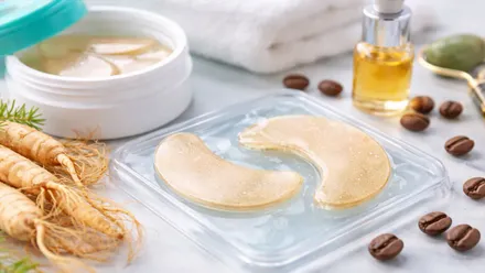 Dos parches para aplicar con un tono anaranjado, cerca hay un tarro de líquido y ginseng.