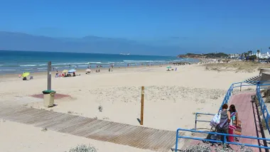 Playa de Chiclana con un suelo parcial de madera, luchas y mucha arena dorada, al fondo el mar en azul.