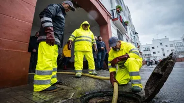 Tres personas observan una alcantarilla en la que una manguera vierte agua.