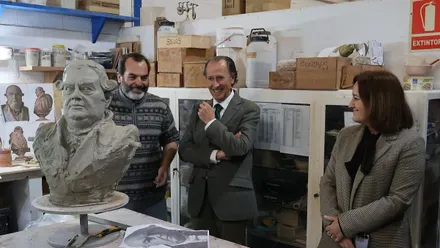 En el taller del artista tres personas, escultor, delegada y alcalde, miran el busto en barro de Alejandro Risso.