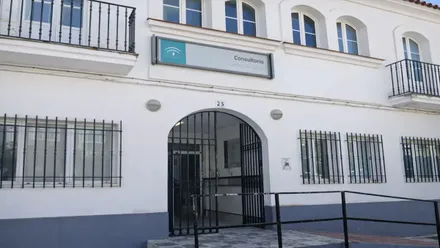 Puerta de acceso al Centro de Salud en Alcalá de los Gazules. Edificio en blanco y la zona baja en gris.