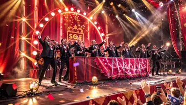 Personas vestidas de negro, como cofrades, cantando una chirigota en el escenario.