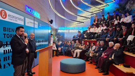 Fotografía del interior del edificio Zona Base Incubazul durante el Torneo Nacional de Debate Económico, con los equipos de estudiantes en pleno debate y el jurado observando al fondo. En primer plano, el delegado Fran González saluda a los participantes junto a representantes del Colegio de Economistas de Cádiz. La imagen muestra la estructura de contenedores marítimos reciclados que caracteriza al espacio, símbolo del compromiso con la innovación y la sostenibilidad.