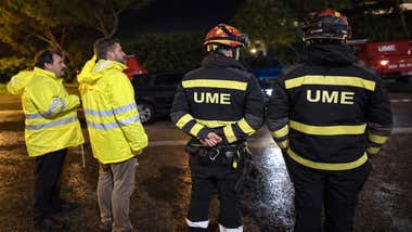 Cuatro personas observan las labores de limpieza en una carretera, dos de ellos son de la UME, otros dos viste indumentaria amarillo fluorescente.