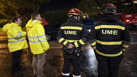 Cuatro personas observan las labores de limpieza en una carretera, dos de ellos son de la UME, otros dos viste indumentaria amarillo fluorescente.