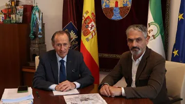 El acalde José María Román en la reunión en una mesa de madera, tras él las banderas, destaca la de España.