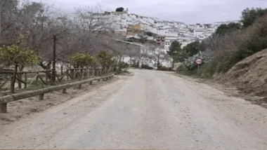 Carretera con mucho barro y al final, sobre una colina se ve el pueblo con sus casas blancas.