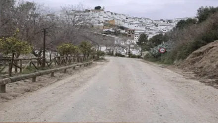 Carretera con mucho barro y al final, sobre una colina se ve el pueblo con sus casas blancas.