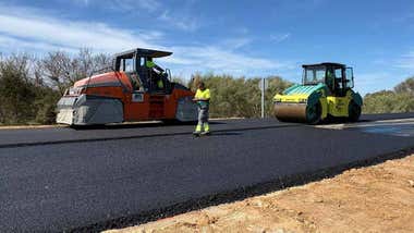 Hormigonera y apisonadora trabajando en una carretera recién asfaltada.
