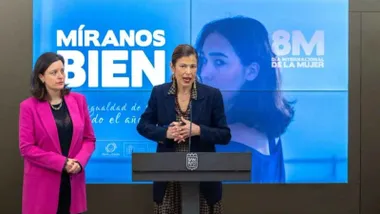 Patricia Cavada con una chaqueta rosa junto a la delegada -de gris-, delante de una pantalla con el 8M.