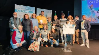 Un grupo de personas posa como parte de AVINSAL en Chiclana. Están delante de una pantalla de guía de aves.