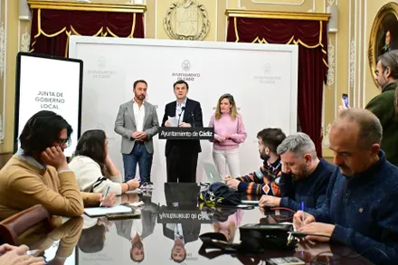 Imagen de la sala de prensa del Ayuntamiento de Cádiz durante la comparecencia posterior a la Junta de Gobierno Local. En primer plano se observa a varios periodistas sentados tomando notas y grabando con sus dispositivos mientras siguen la rueda de prensa. En un atril interviene el alcalde de Cádiz, Bruno García.
