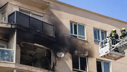 Escalera mecánica con dos bomberos frente a la ventana quemada del piso en Algeciras.