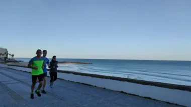 Dos hombres y una mujer corren por el Paseo Maritimo de Cádiz bajo un cielo azul en una mañana fresca del 30 de marzo