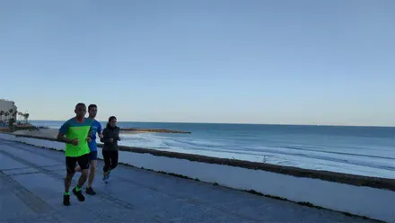 Dos hombres y una mujer corren por el Paseo Maritimo de Cádiz bajo un cielo azul en una mañana fresca del 30 de marzo