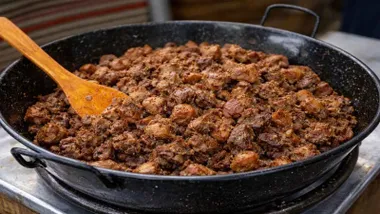 Perol negro con cochinillo y un cucharón de madera.