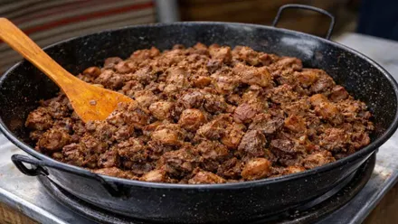 Perol negro con cochinillo y un cucharón de madera.