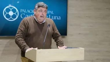 Manrique en pie en un atril con una pantalla azul tras él.