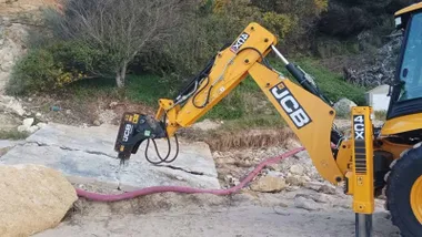 Pala excavadora moviendo o rompiendo una loza de piedra.