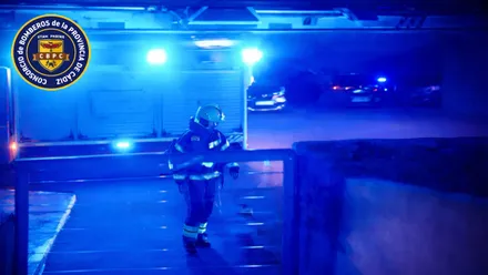 Bombero delante de un camión de la unidad con luces azules encendidas.
