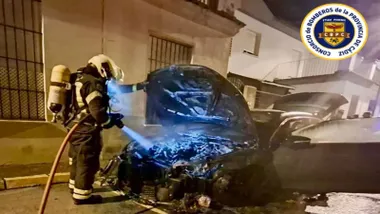 Bombero iluminando la parte del motor de un coche carbonizado.