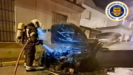 Bombero iluminando la parte del motor de un coche carbonizado.