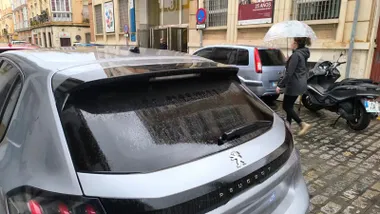 Una mujer pasa con un paraguas por detrás de un coche mojado en Cádiz