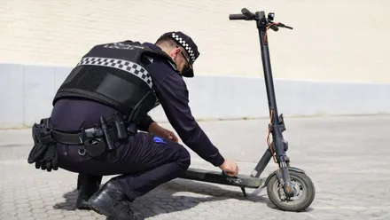 Policía local de azul agachado y verificando un patinete gris-negro.