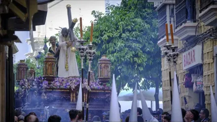 El Nazareno del Amor avanza sobre su paso por una estrecha calle de Cádiz, rodeado de público y penitentes con capirotes blancos, entre el humo del incienso.