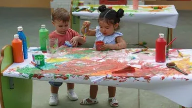 Dos niños coloran en papeles embadurnados de pintura.