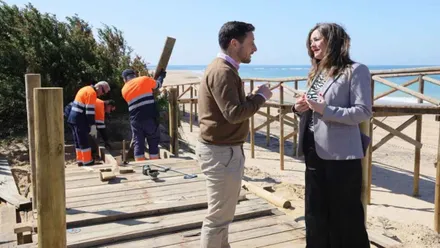 Operarios trabajan en uno de los postes de la playa mientras los concejales conversan.