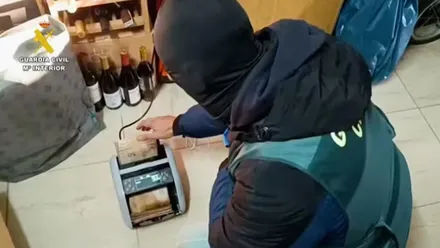 Guardia Civil agachando contando billetes de 50 euros en una contadora.