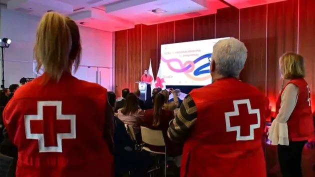 Tres personas de la Cruz Roja miran al atril.