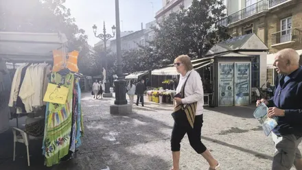 Dos personas pasean por la plaza de las Flores de Cádiz con los puestos montados y en una jornada soleada