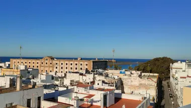 La Caleta con el Castillo de San Sebastián y el faro, el edificio del Hospicio el y el arbol del Mora bajo un cielo azulísimo en Cádiz.