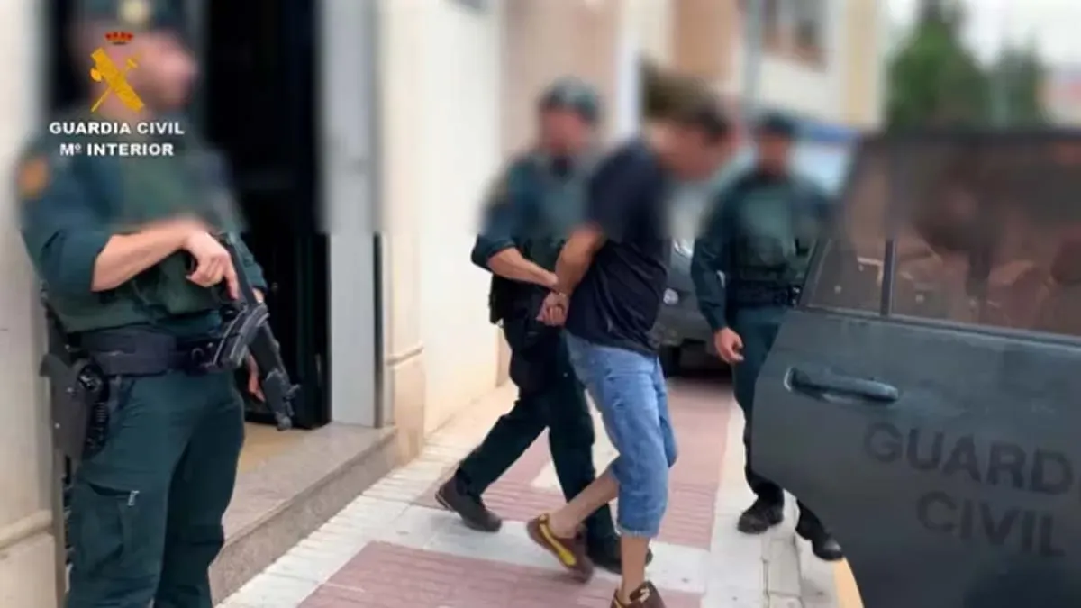Agentes de la Guardia Civil conducen a un detenido al un vehículo, va esposado.