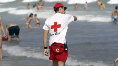 Socorrista a la orilla de la playa con camiseta blanca y gorra roja con logotipos de Cruz Roja.