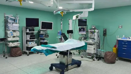 Mesa de operaciones e instrumental y aparatos de un quirófano. Destacan las paredes en un tono suave de verde.