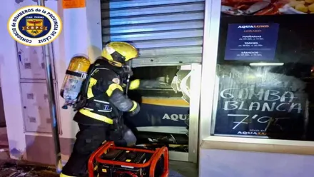 Bombero tratando de acceder al interior del local incendiado.