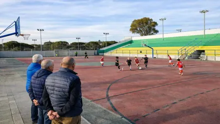 Niños jugando y tres ancianos mirando en una pista deportiva.