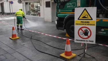 Un camión verde de la limpieza de San Fernando y un operario retirando la cera de la Semana Santa.