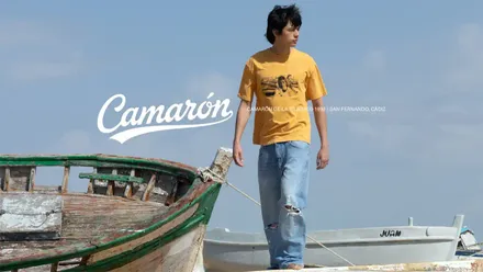 n modelo posa con una camiseta d ela colección 'Volando voy' entre barquitas mientras se ve en la imagen la palabra Camaron y "Camaraon 1950-1992. San Fernando"
